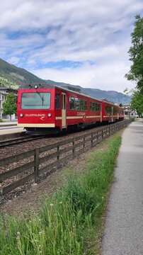 Zillertal, Austria: 10.5.2026: Red Zillertalbahn passenger train traveling on curved railway tracks through the scenic alpine valley of Zillertal in Tyrol, Austria. Dramatic clouds, green hills and pe