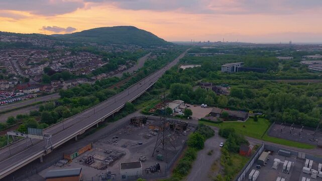 Motorway at Sunrise with Houses on Hill with nearby Substation and BESS Battery Energy Storage System installation made of lithium-ion. Modern green energy infrastructure. South Wales, UK.