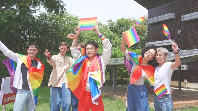 Pride and LGBTQ concept. A group of LGBTQ people dressed up, carrying rainbow signs and flags, dance and celebrate happily at a Pride festival event in the park.