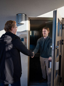 Smiling man greeting male maintenance worker with handshake while standing at doorway of house
