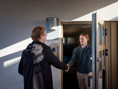 Smiling man shaking hand with male maintenance worker while standing at doorway of house