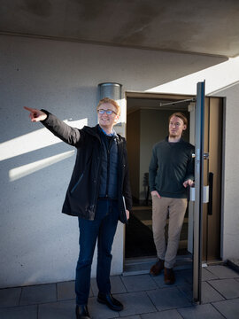 Smiling male snow warden pointing while talking with man standing at doorway of house
