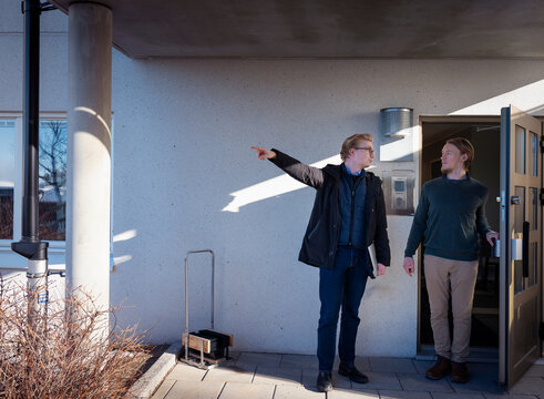 Male snow warden pointing while talking with man standing at doorway of house