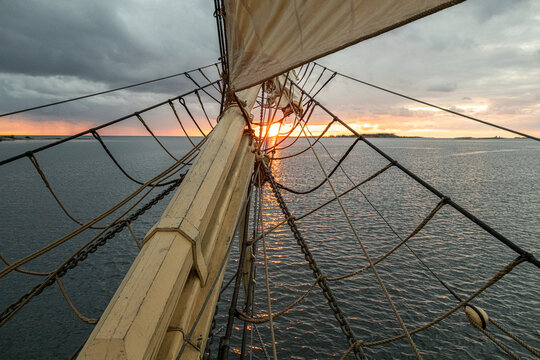 Tall ship's rigging and mast seen against scenic sea under cloudy sky at sunset