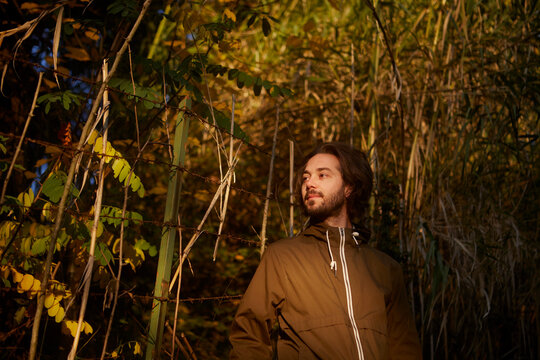 Contemplative man looking away while standing near fence in forest