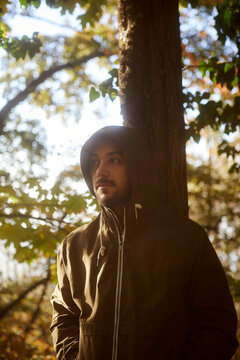 Man wearing hoodie looking away while standing near tree in forest