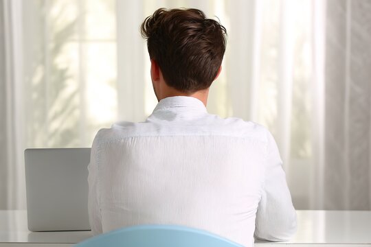 Rear view of young man sitting at desk with laptop