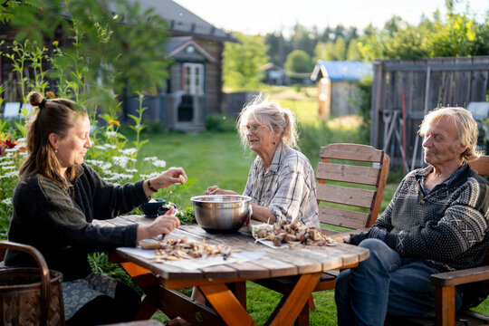 Senior parents sitting with daughter peeling potatoes while sitting at table in back yard
