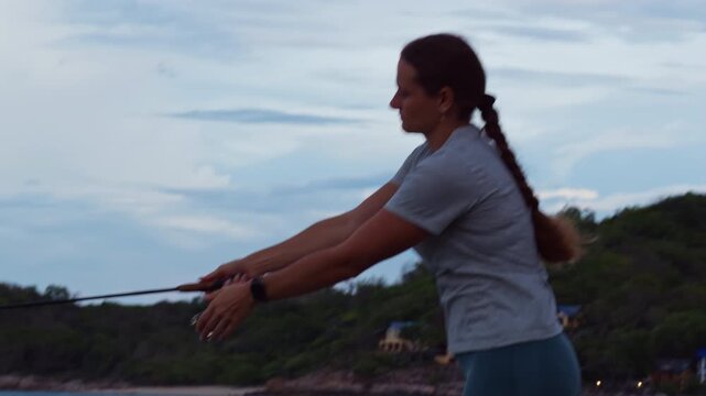 Side View of Young Woman Casting Spinning Rod Near Tropical Coastline and Forest Under Evening Sky, Slow Motion Outdoor Fishing and Adventure