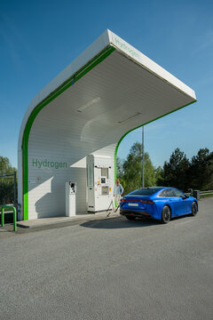 Woman standing near electric car getting charged at hydrogen refueling station on roadside against clear sky