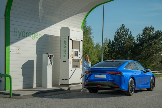 Female charging hydrogen fuel cell electric car at roadside station on sunny day
