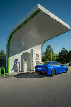 Woman standing at station while hydrogen fuel cell electric car getting charged on sunny day