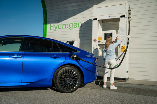 Rear view of woman operating machine while charging electric car at station on sunny day