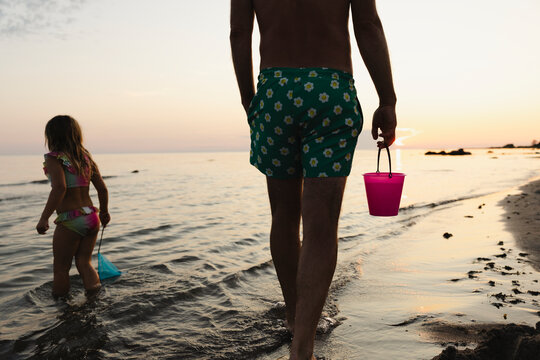 Rear view of father holding bucket while spending leisure time with daughter at beach