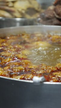 Vertical view shows Bun Mang Vit soup boiling in a large metal pot during cooking at a local outdoor trading location with vendor preparation activity. Everyday cooking.