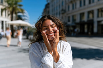 Fototapeta premium Delighted Woman in Bustling City Applying Sunscreen on Face, Joyful SPF Skincare Moment, Urban Outdoor Sun Protection Routine, Spontaneous Lifestyle and Healthy Skin Care Awareness