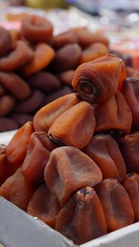 Vertical view shows dried persimmons arranged in multiple rows on a retail counter forming a structured display inside a neighborhood trading area. Market culture.