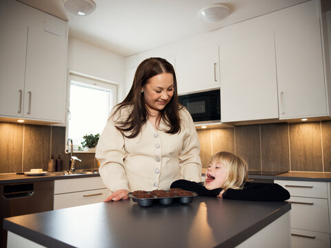 Playful girl standing with mother near muffin tin kept on table at home