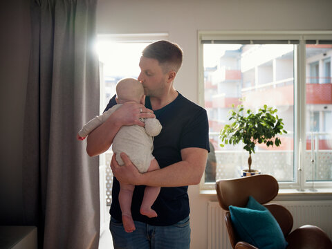 Man kissing toddler son while embracing him in living room at home
