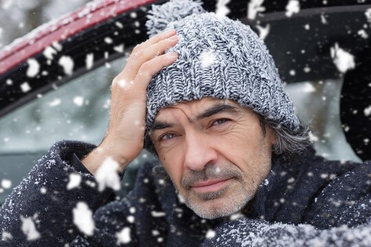 Tired male driver looks into rearview mirror during snowfall