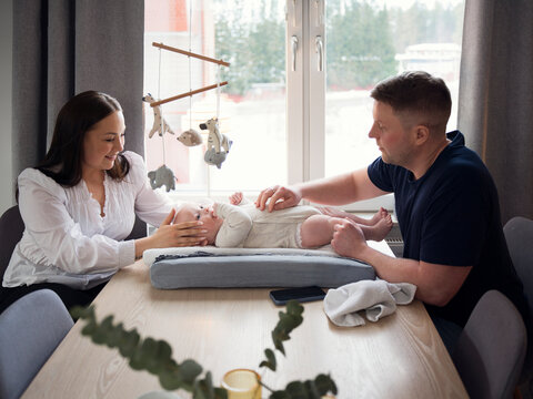 Parents spending leisure time with baby boy lying on small bed at table in home