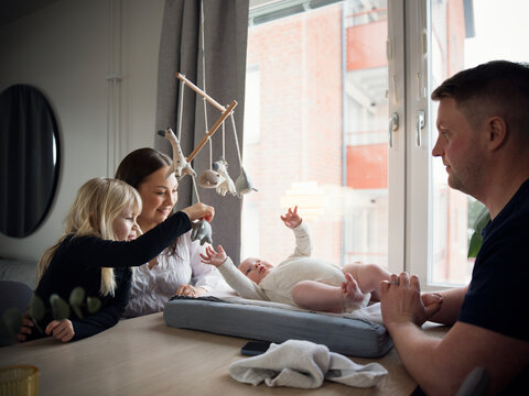 Parents spending leisure time while daughter playing with baby brother at home