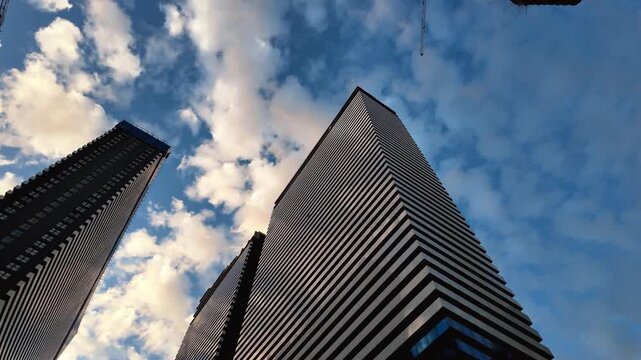 Modern skyscraper towers reaching towards a partly cloudy blue sky, with a slow pan revealing a new building under construction next to the finished contemporary office and residential buildings