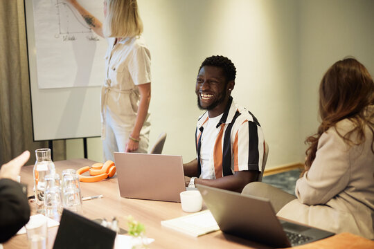 Happy male employee laughing while sitting with colleagues in office meeting