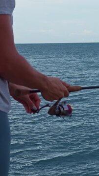 Vertical video. Close View of Young Woman Holding Spinning Reel and Fishing Rod Above Tropical Ocean Under Evening Sky, Slow Motion Recreational Fishing