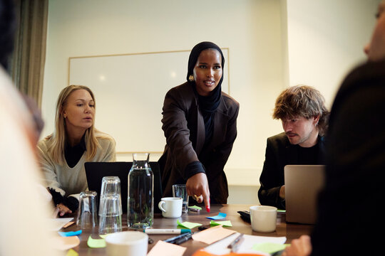Businesswoman pointing at adhesive note while interacting with team in meeting room