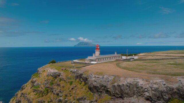 Cinematic Drone Reveal of Farol de Albarnaz Lighthouse on a Rocky Cliff with Corvo Island on the Distant Horizon