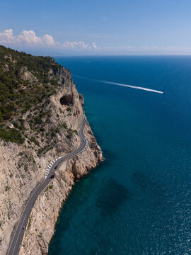 Aerial view of the winding coastal road along the steep cliffs of Sentiero del Pellegrino overlooking the turquoise Mediterranean Sea Noli, Liguria, Italy.