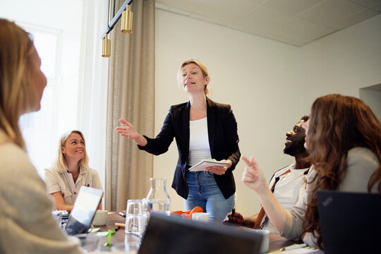 Female manager holding diary and interacting with colleagues in team meeting
