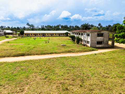 Aerial view of school buildings and a grassy courtyard with children playing under a cloudy sky in Ahoada I, Rivers, Nigeria.