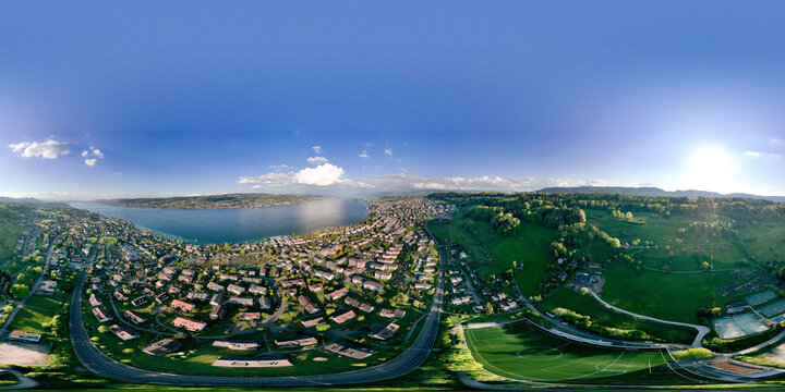 Aerial view of the residential area of Thalwil overlooking Lake Zurich with green hills and a football field under a clear blue sky Thalwil, Zurich, Switzerland.