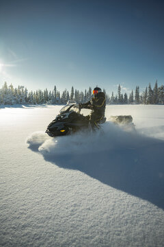 Shot of person riding black snowmobile across flat snow field