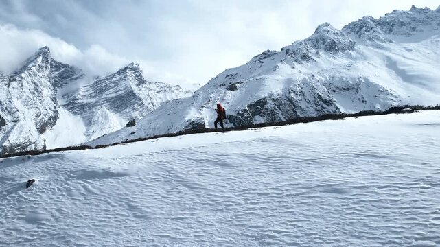 Cinematic footage of a trekker in a red jacket walking along a snow-covered trail with dramatic Himalayan peaks rising behind in Nepal's Manaslu region.