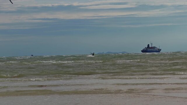 Distant Kitesurfer Riding Across Stormy Tropical Sea Near Cargo Ship Under Dramatic Cloudy Sky, Slow Motion Extreme Water Sport Adventure