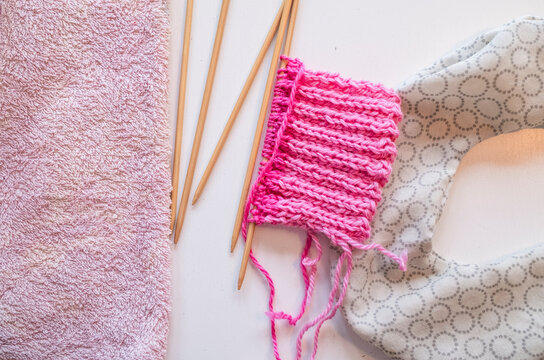Small piece of pink yarn on white table next to wooden needles