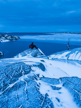 Shot of person looking at frozen lake while sitting on rock