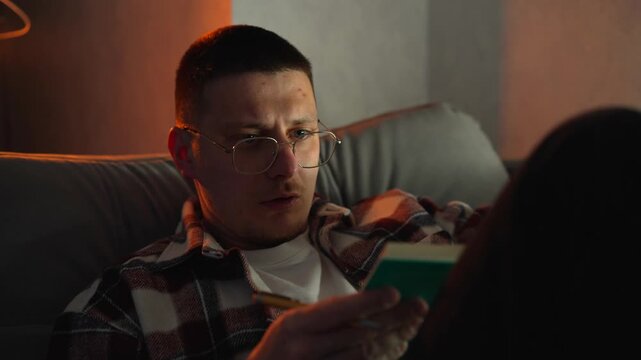A man reading a book in the bedroom in the evening before going to bed