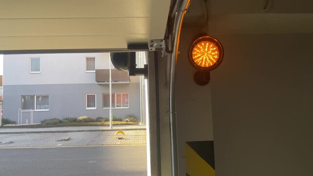 Amber flashing safety light under garage ceiling. Mounted on doorframe with spiral LED pattern, concrete interior, dusk exterior visible through opening,