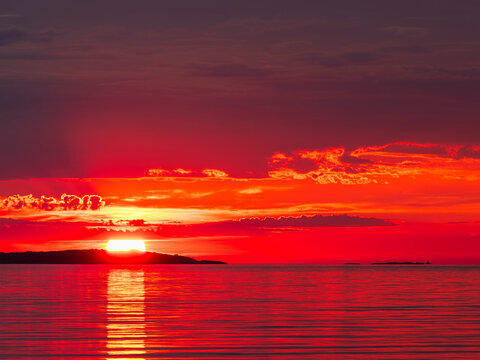 Bright red sun setting over calm sea with dark islands