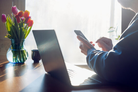 Male freelancer using phone while sitting with laptop at home