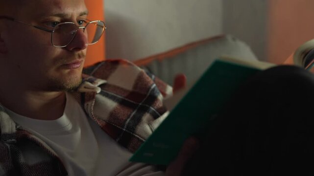Reading a book in a cozy home atmosphere sitting on the sofa in the evening