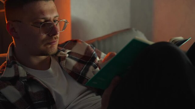 A man reads a book and turns over the paper pages.
Interesting literature and detective stories in a homely evening atmosphere.
