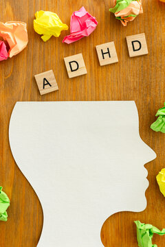 Silhouette of a head with the letters ADHD neatly arranged inside, surrounded by crumpled papers, on a wooden table