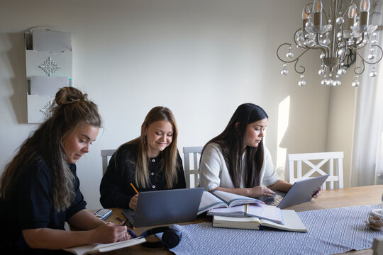Woman sitting with teenage girls studying while sitting at table in living room of home