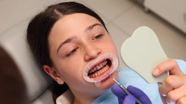 Teenage girl examining her dental braces in a mirror at the orthodontist