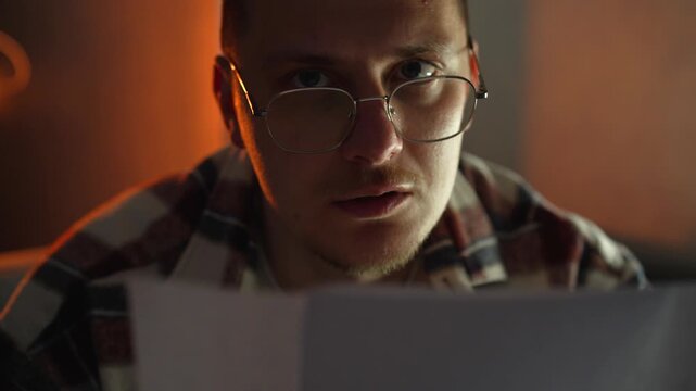 A student reads something on a white sheet of paper, preparing for a college exam.
He sits in a dark room in the evening, carefully studying the questions.